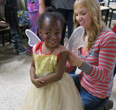 toddler girl dresses as angel with adult helping with costume