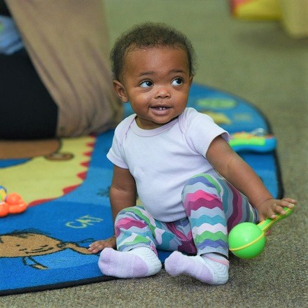 toddler sitting with rattle, looking to the side