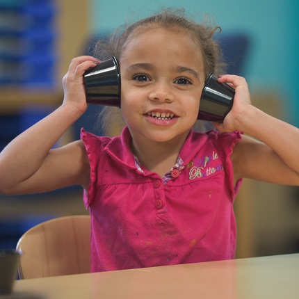 preschooler with holding cups to her ears